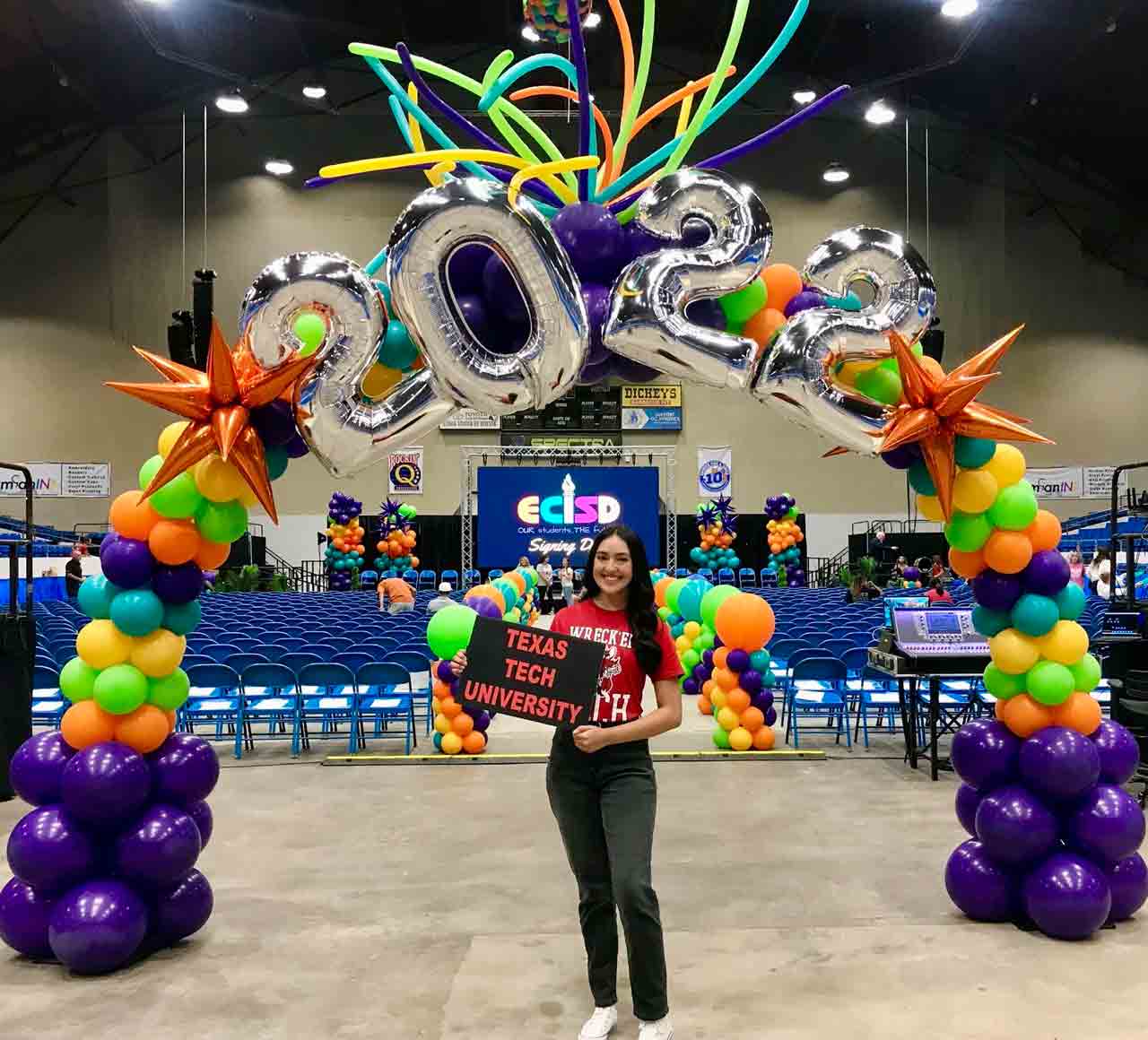Lizeth Rios poses under a balloon arch holding a Texas Tech University sign