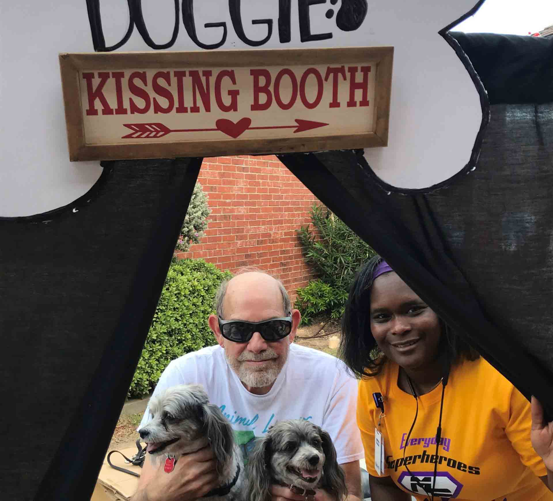 People holding their dogs under a doggie kissing booth sign