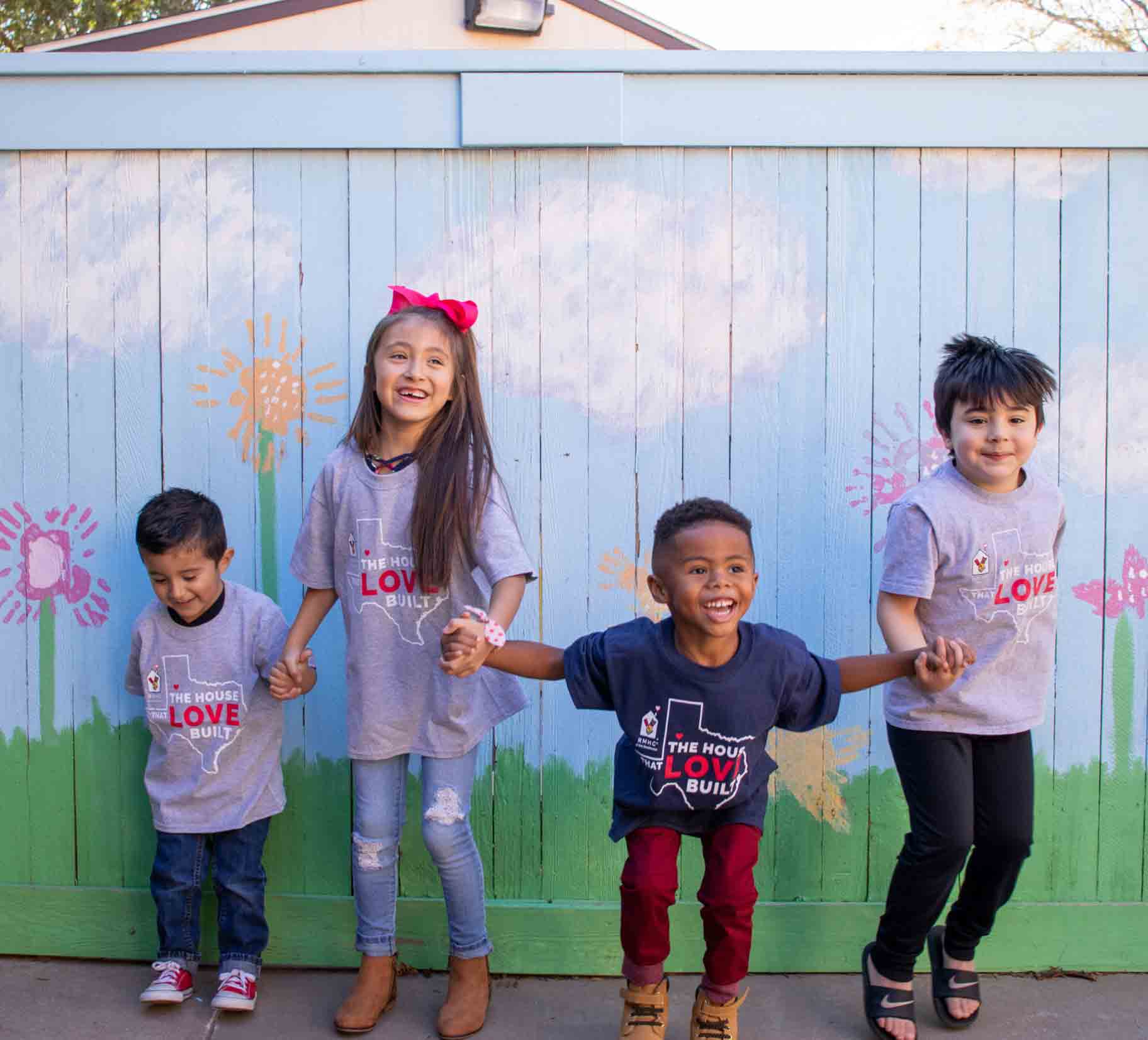 Children holding hands in front of a colorful painted fence